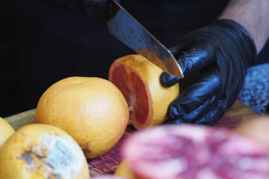 Hands slice a vibrant grapefruit on a wooden board surrounded by citrus.