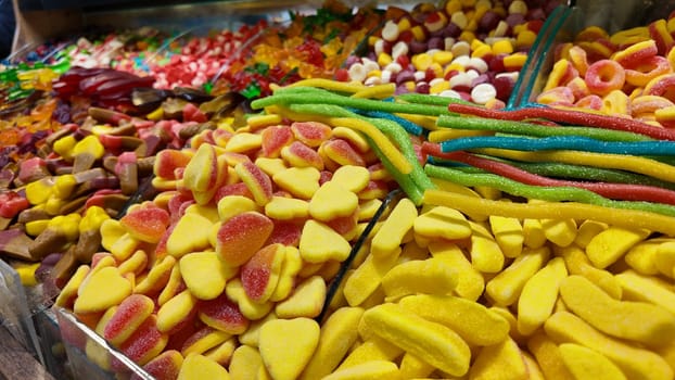 A vibrant display of various gummy candies fills a market stall.