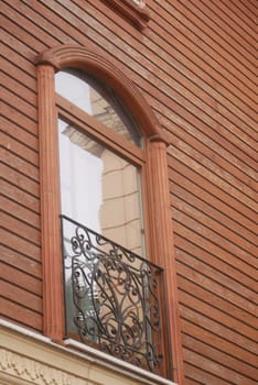 Ornate balcony frames a beautiful window in a brick facade building.