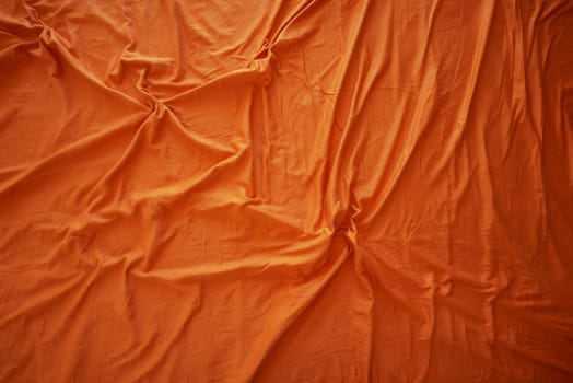 Bright orange fabric displays a textured surface with soft folds and wrinkles.