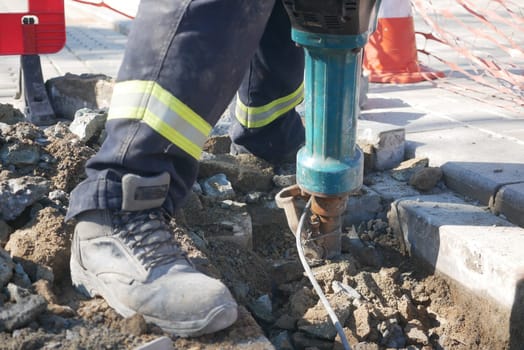 Worker operates a jackhammer to break concrete during urban repairs.