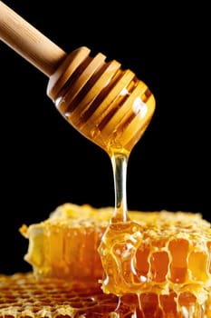 A wooden dipper slowly pulls honey from a honeycomb, revealing a rich amber hue. The sticky liquid glistens under the light, highlighting its smooth texture.