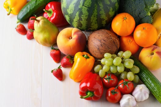 A variety of fresh fruits and vegetables such as watermelon, oranges, strawberries, and bell peppers are artistically arranged on a light wooden surface.