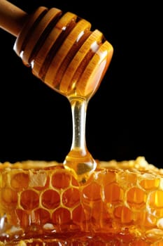 Golden honey is slowly dripping from a wooden dipper into a honeycomb structure with a dark background, highlighting the rich texture and color of the natural sweetener.