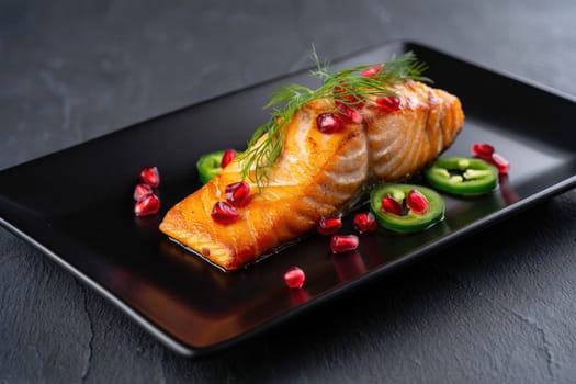 A beautifully plated grilled salmon fillet garnished with fresh dill, pomegranate seeds, and spicy jalapeño slices.