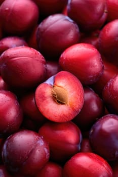 A vibrant collection of plums displays a rich variety of red hues. Droplets of water cling to their shiny skin, enhancing their appetizing appearance and indicating freshness.