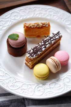 A beautifully arranged plate features an array of pastries including layered cakes and colorful macarons. The desserts showcase a variety of textures and flavors, perfect for a sweet afternoon treat.