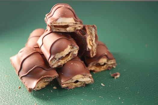 Chocolate-covered snack bars are stacked artfully on a green surface.