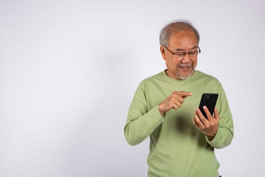 Portrait smiling Asian older man smiling and pointing at his cell phone studio shot isolated on white background. elderly holding mobile phone in hand. Concept of connection and communication