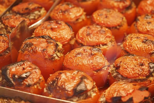 Stuffed tomatoes are arranged in a warm display at a bustling market stall.