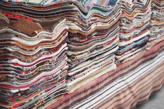 Stacks of colorful turkish textiles displayed at a market in the afternoon.