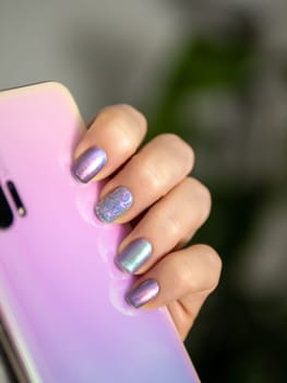 Stylish Iridescent nail art manicure. Female hand with skittles nails holds smartphone. Spring and summer glowing nail art design ideas.