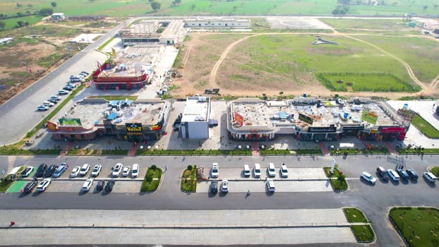 Delhi, India - 19th Feb 2025: Panning sideway aerial drone shot showing mix of branded food outlets in rest area midway of delhi Mumbai expressway with cars parked and huge green parks in distance showing rapid development in road network by NHAI