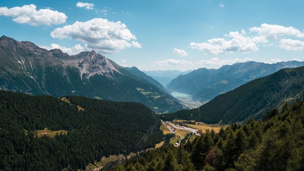 sweeping view from Alp Grum overlooking Poschiavo Valley, with alpine peaks, green forests, and a distant lake under a clear blue sky. A peaceful Swiss mountain summer scene