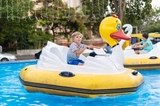 Child riding inflatable duck-shaped paddle boat on a shallow pool at an outdoor amusement park attraction