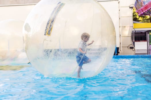 Boy in a striped shirt inside an inflatable water walking ball on a pool at an amusement park or fairground