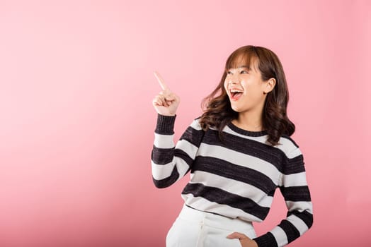 Asian happy portrait beautiful cute young woman standing makes gesture two fingers point upwards above presenting product something, studio shot isolated on pink background with copy space