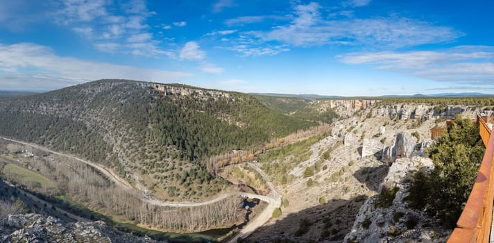A panoramic view of a rugged mountain valley with forests, a winding river, and a clear blue sky conveys tranquility and adventure.