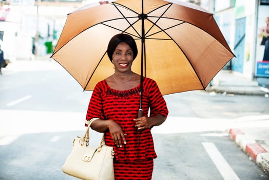 mature woman in traditional clothes standing outdoors looking at camera smiling with umbrella over her head