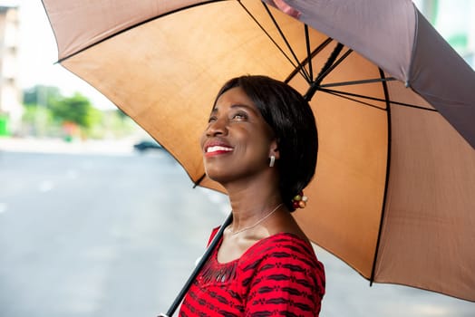 Portrait of a beautiful African adult businesswoman dressed in red loincloth holding an umbrella in hand looking up