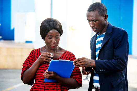 handsome man and beautiful african adult businesswoman standing by discussing project business, holding in hand a blue document and a drink, on the street