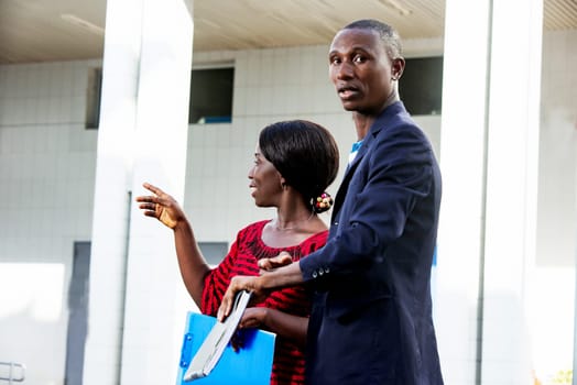portrait of beautiful businesswoman and african adult businessman, standing side view, using document in hand, on the street