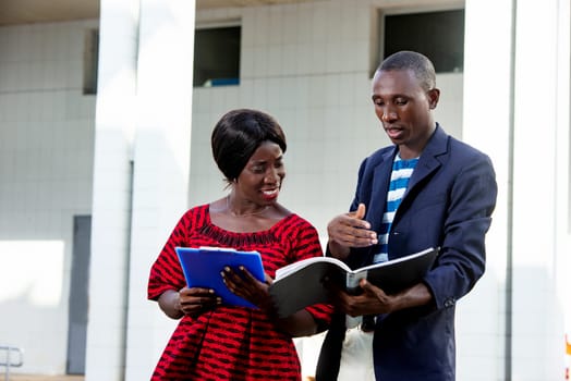 handsome african businessman and beautiful african woman, working outdoors with documents and folders, in front of office building outdoors