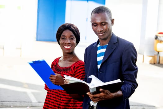 beautiful woman and handsome african adult businessman standing smiling, talking and displaying documents in the street