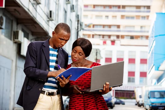 Confident african businessman pointing at a document explaining, the specific project has his assistant on the street while smiling