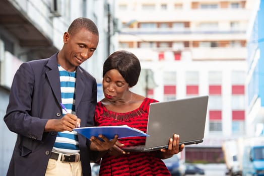 Confident african businessman pointing at a document explaining, the specific project has his assistant on the street while smiling