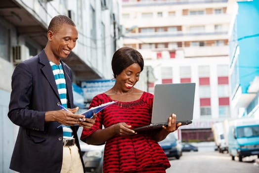 Photo of handsome man and beautiful woman as business partners outside holding in hand a computer and folder while smiling