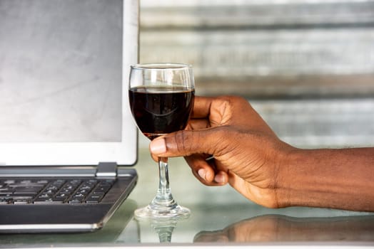 holding a glass of red wine by an African American adult man with finger shot and nails near a computer