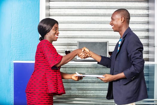 Professional business woman and man in formal suit shaking hands outside to make an agreement exchanging documents while smiling