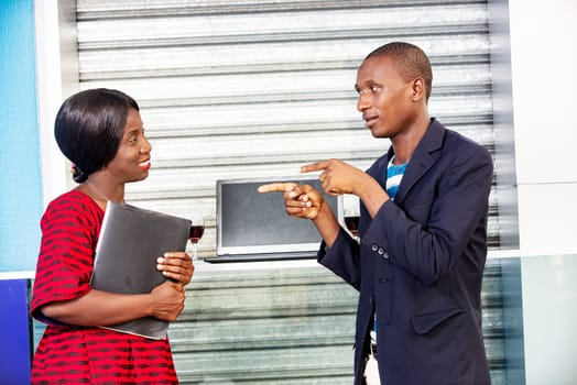 handsome african man pointing at african businesswoman holding laptop in hand on street
