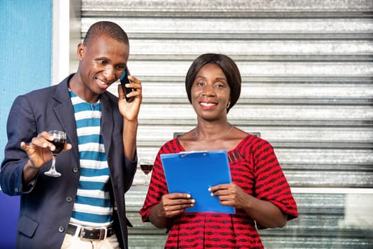 beautiful African secretary holding a document while smiling, while the businessman telephoning with a glass of red wine in hand