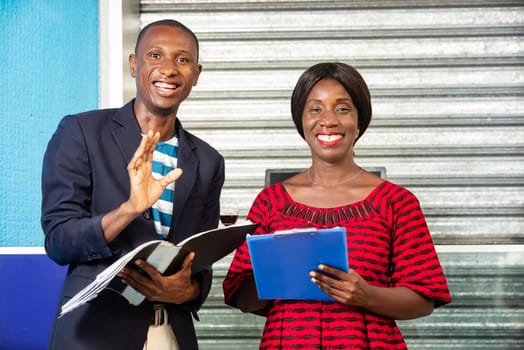 handsome businessman and businesswoman each holding a document outside while being smiling