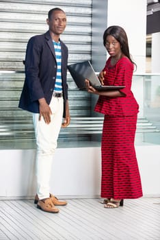 Photo of handsome businessman and beautiful woman as business partners outdoors holding a computer while smiling