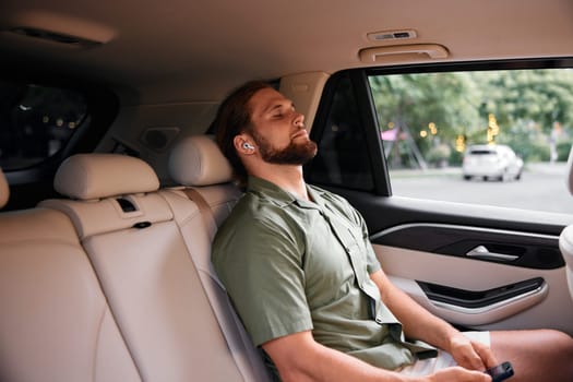 A stylish young man enjoying his time in a car s back seat, displaying a calm demeanor with wireless earbuds in, surrounded by a serene, blurred urban environment