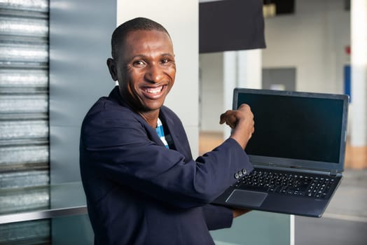 handsome adult businessman making a gesture pointing to show a laptop while being happy on the street