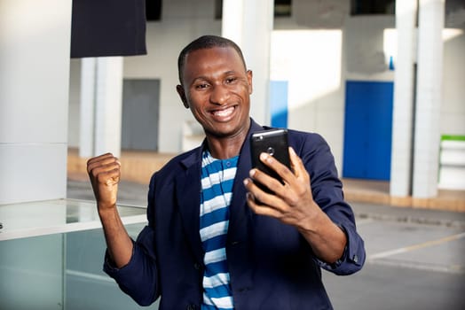 handsome happy adult business man looking at his phone while making a victory gesture with the outside hand