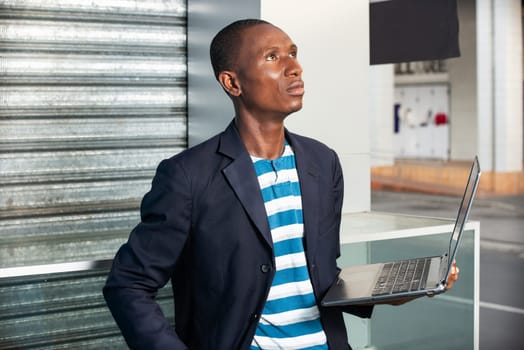 handsome adult businessman holding computer hand is thinking while looking up at the sky outdoors in the street