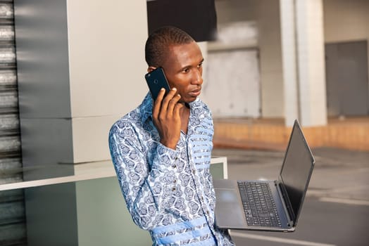 young businessman standing outdoors talking on mobile phone and holding laptop.