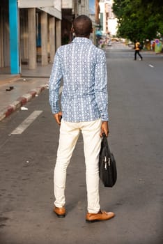 young businessman standing outdoors looking back at the camera and holding a bag.