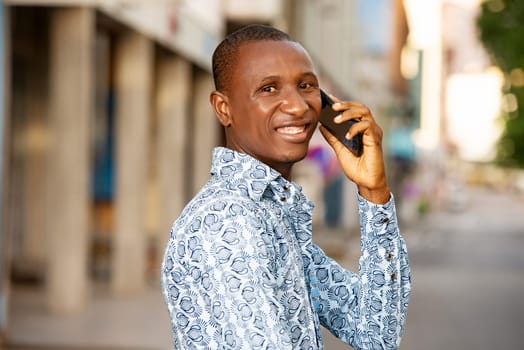 young businessman standing outdoors talking on mobile phone and looking in profile smiling.