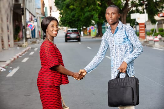 young businessman standing outdoors in traditional dress shaking hands with his partner smiling.