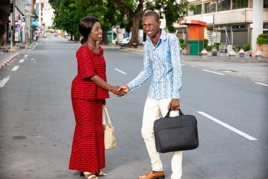 young businessman standing outdoors in traditional dress shaking hands with his partner laughing.