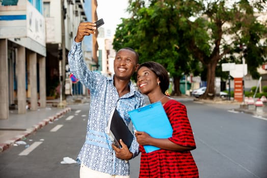 african business people smile while looking at a funny photo or watching a video on the mobile phone with documents in hands outdoors