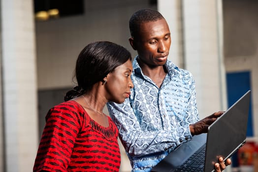 Young african businessman showing project plan pointing finger on laptop screen with woman smiling on street