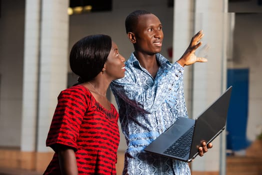 Young businessman discussing work using a laptop with a woman outdoors in town.