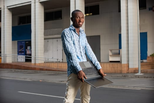 Happy african adult man standing smiling using a laptop in hand on the street